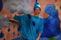 Na zdjęciu aktorka grająca kroplę wody w przebraniu, za nią scenografia- przedstawiająca chmury i deszcz.