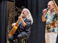 Dwóch artystów na scenie, jeden śpiewa, drugi gra na instrumencie.