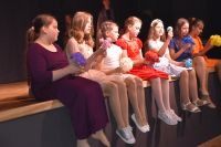 Młode aktorki siedzą na krawędzi sceny i recytują.